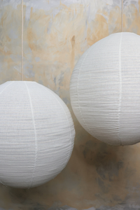 Two white spherical linen lanterns hanging against a textured wall.