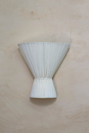 An off-white textile wall light sconce mounted on a wall, with a conical shape and pleated texture.