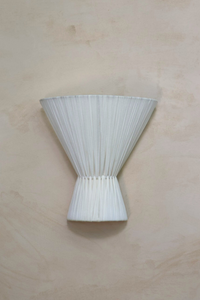 An off-white textile wall light sconce mounted on a wall, with a conical shape and pleated texture.