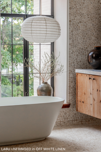 A white linen pendant light shade with a rattan frame, hanging and displaying a textured surface.