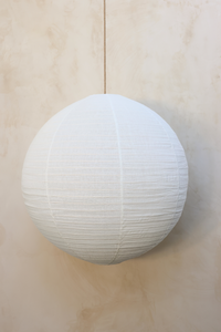 A round linen light shade with a woven rattan frame, hanging against a neutral background.