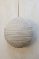 A round linen light shade with a woven rattan frame, hanging against a neutral background.