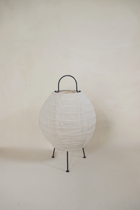 A Desa linen table lamp with a natural rattan body and a white linen shade, standing on a minimalist tripod base.