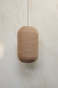 A bronze color linen shade designed for pendant lighting, displayed against a wooden background.