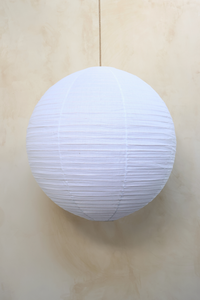 A white round linen light shade with a woven rattan frame, hanging against a neutral background.