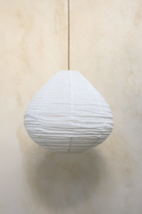 A pear-shaped linen light shade hanging against a wooden background, with a fringed design.
