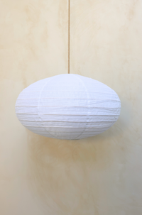 A beige linen dome pendant shade hanging against a wooden background.