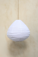 A pear-shaped linen light shade hanging against a wooden background, with a fringed design.