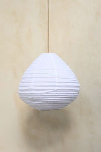 A pear-shaped linen light shade hanging against a wooden background, with a fringed design.